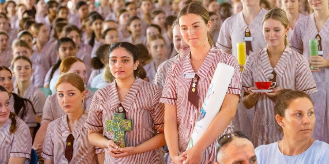 Students in school uniforms standing together during an assembly holding books and awards